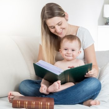 Beautiful young mother reading big book to her smiling baby boy