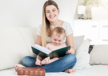 Portrait of adorable baby boy sitting on mothers lap and looking at big book