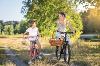 Happy girl riding on bicycle with her mother in meadow at sunset