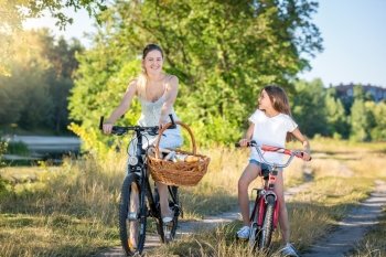 Beautiful young mother cycling with daughter riding to picnic