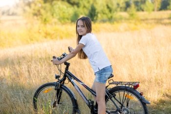Portrait of beautiful teenage girl sitting on bicycle at meadow