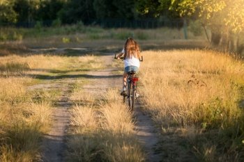 Young woman riding bicycle on dirt road at meadow