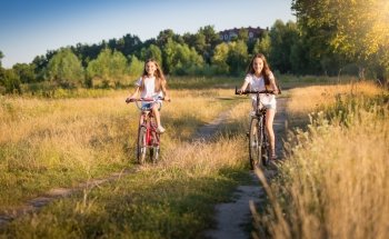 Two beautiful girls riding bicycles on meadow at sunny day