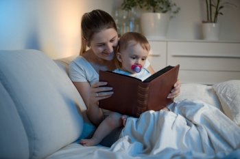 Portrait of smiling mother and adorable baby reading book before going to sleep a night
