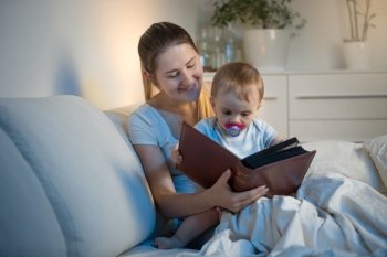 Portrait of beautiful young mother reading book to her baby before going to sleep
