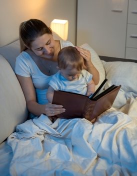 Portrait of beautiful smiling mother reading story to her baby boy before going to sleep