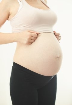 Closeup photo of pregnant woman in sportswear showing big belly