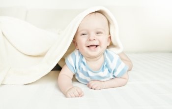 Cute laughing 6 month baby boy lying under the blanket on bed