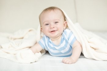 Portrait of happy little baby crawling on bed under blanket