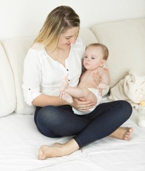Beautiful young mother sitting on bed with her cute baby boy
