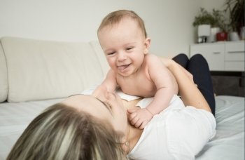 Portrait of young smiling mother lying on bed and playing with her 6 month son
