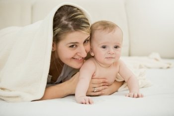 Toned portrait of happy young mother lying with her baby son under blanket