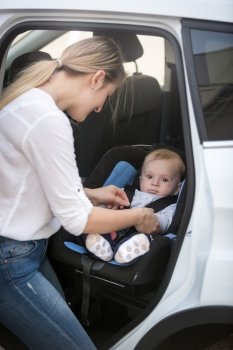 Young mother seating her baby in car safety seat