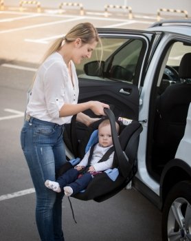 Portrait of young mother installing car child seat with baby