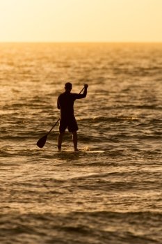 Man paddleboarding in open water at sunset
