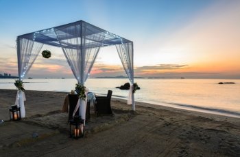 Romantic dinner table with white tent for a couple on tropical beach at twilight