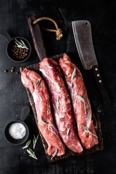 fresh raw pork tenderloin on wooden cutting board on dark background
