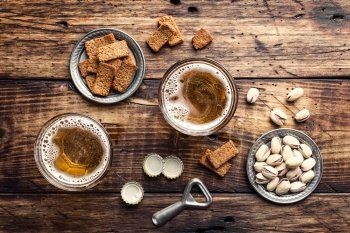 Two glasses of fresh beer and salty snacks on a brown wooden table, top view 