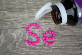 Pink pills forming shape to Se alphabet on wood background
