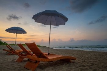 Orange beach chairs and parasols on sandy beach with morning sky and sea
