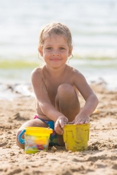 Glad kid playing on a sandy beach with a pond and sand molds