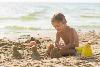 The child sits on the sandy beach of the reservoir and enthusiasm molds of sand cakes