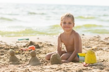 The child sits on the waterfront and sculpts sand cakes