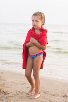 Frozen five year old girl wrapped in an adult t-shirt standing on a sea shore