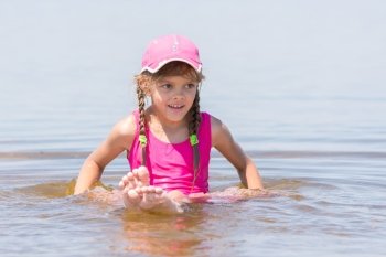 Girl in a cap sits on a shallow river in water