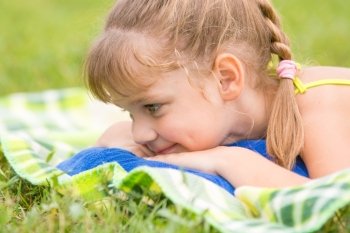 Five-year girl lies on a green meadow and touching looking at grass