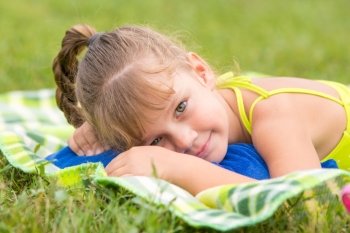Five-year girl lies on a green meadow and touching looking to the frame