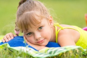 Five-year girl lies on a bed on a green meadow and touching looking to the frame