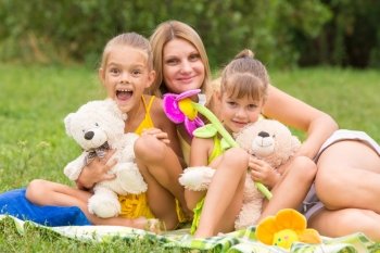 Mother and two daughters sitting with soft toys on a picnic