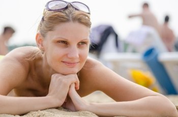Young girl lying on the sandy beach against the backdrop of other travelers and smiling looks into the distance