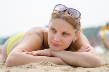 Sad young girl lying on sandy beach and looking to the side
