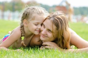 Five-year cute daughter pressed her face to the mother's face on a green grass lawn