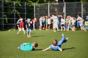 Two young little boys lie on grass at football stadium. Summer outside