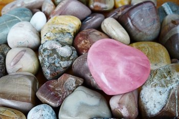 rose quartz heart on multicolored background sea pebbles