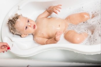 Little pretty wet baby boy in bath room lying on white background, horizontal picture.