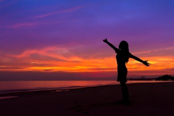 Silhouette of woman with hands up while standing on the sea beach at sunset