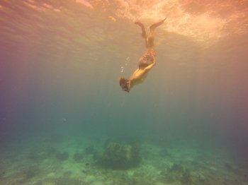 Underwater selfie shot with young man diving on a breath hold in a tropical sea over sandy bottom. Deep blue sea. Wide angle shot. Vintage filtered image.