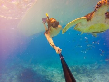 Underwater selfie shot with selfie stick. Underwater marine wildlife postcard. A turtle sitting at corals under water surface. Deep blue sea. Wide angle shot.