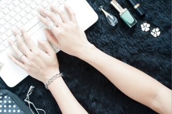 Beautiful woman's hands shopping online on white laptop with her beauty items on black