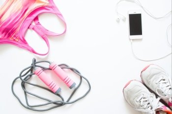 Flat lay of cellphone, pink sport bra, jump rope and sneaker on white background, Working out and healthy concept, top view
