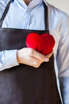 Servicing man in apron holding heart - customer relationship and service minded business concept. Servicing man in apron holding heart - customer relationship and service minded business concept.