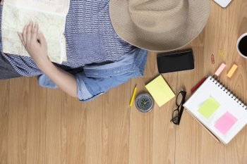 woman lying on wooden floor with hat, mobile phone, notebook and map