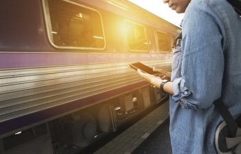 young woman holding mobile phone with backpack standing on platform at train station - travel concept