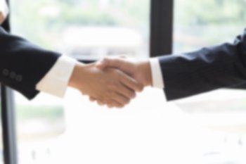 two businessman shaking hands beside window - business teamwork, cooperation concept  - blur for use as background