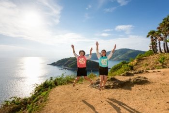Two girls mother and daughter jumping with happy on the mountain at panoramic ocean and island viewpoint of Cape Phromthep in Phuket, Thailand