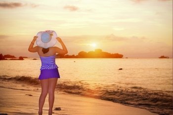 Visitors woman in a blue swimwear and hat standing looking the beautiful landscape of sky over the sea happily on the beach during sunrise at Koh Miang Islands, Mu Ko Similan National Park, Phang Nga, Thailand